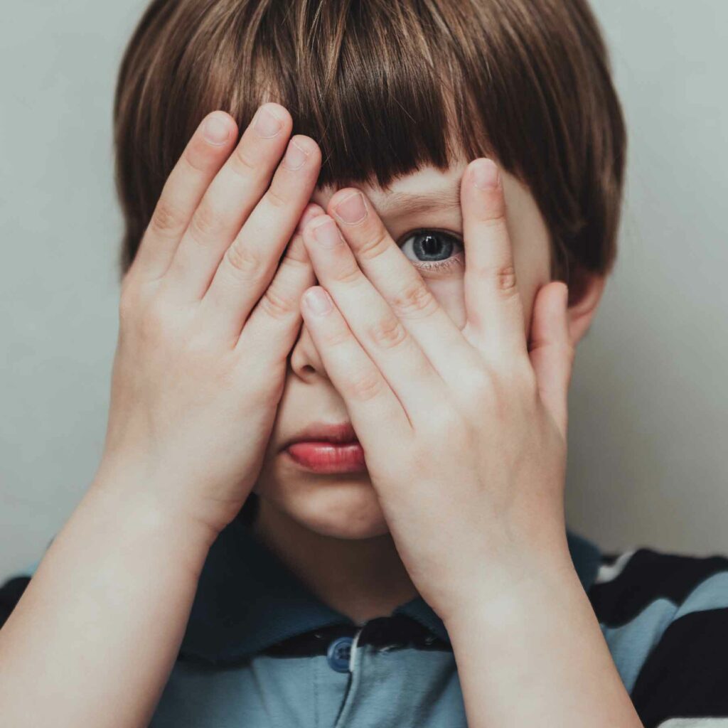adhd-eye Close-up of a child peeking through fingers with a concerned expression, representing vision challenges in children.