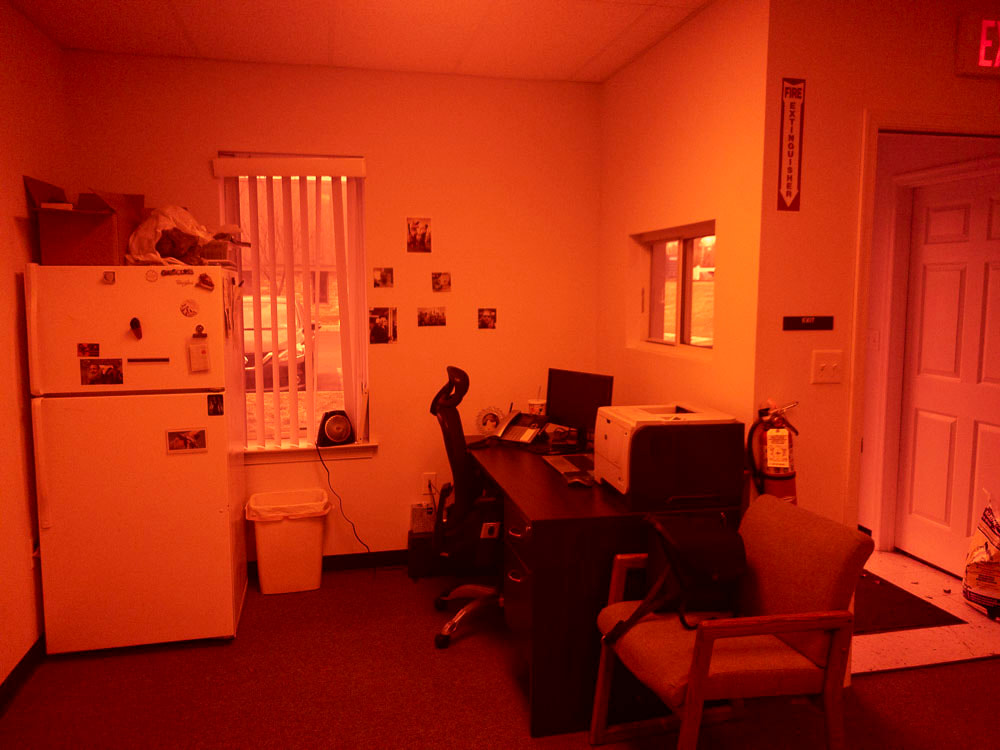 A view of an office room under a deep red tint, applied by the 550x filter, casting a strong red hue over the scene, which intensifies the warmth and alters the visibility of room details by muting cooler tones.