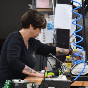 lab_manager_chadwick_optical Lab manager Susan focused on her task at a workbench with tools and equipment in a workshop setting.