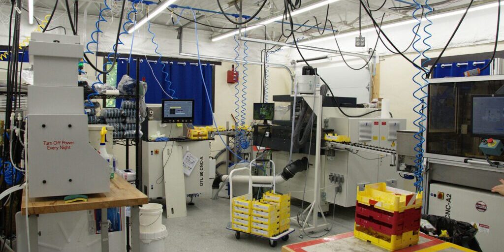 Manufacturing_Chadwick_Optical Industrial lab setup with multiple machines, hanging cables, and yellow storage bins, showcasing a manufacturing environment.