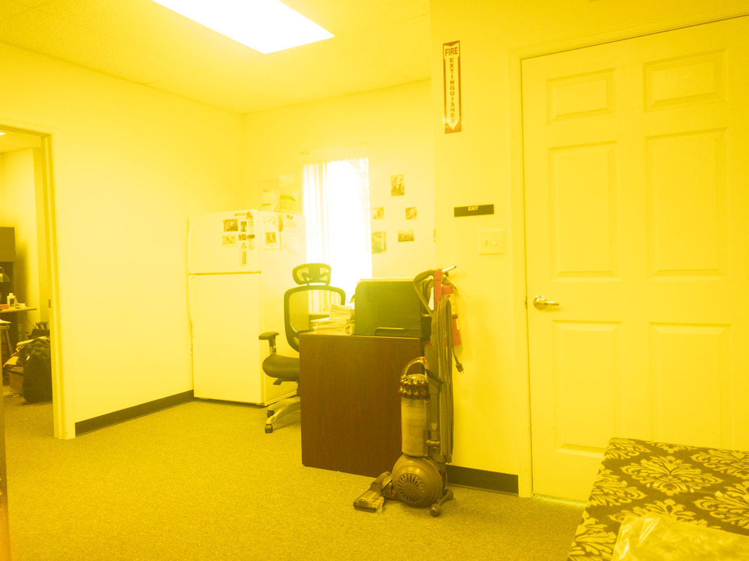 The room seen through the Noir 50 tint, providing a slightly milder yellow overlay that casts a warm tone over the office furniture, making details appear softer but still clear.