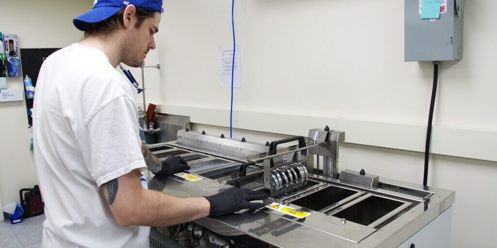 thin_film_coating_Chadwick_Optical Man in a blue cap and gloves operates an ultrasonic cleaner at Chadwick Optical.