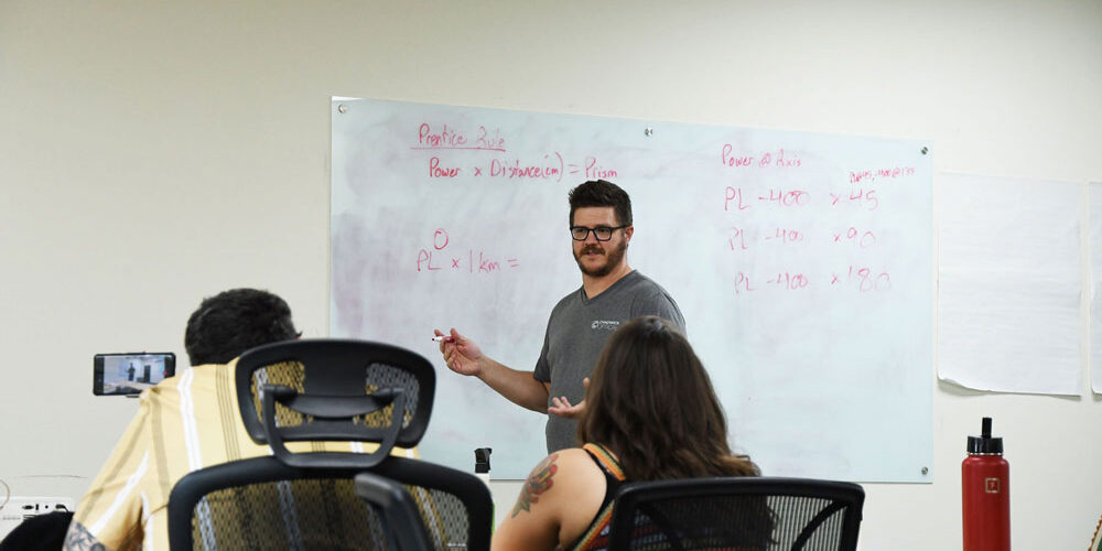 training_chadwick_optical Charlie leads a training session at Chadwick Optical, explaining equations on a whiteboard to a group of engaged employees.