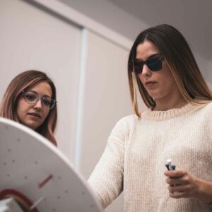 vt Two women engaging in a vision training exercise, one wearing tinted glasses and holding a pointer tool, with focused expressions.