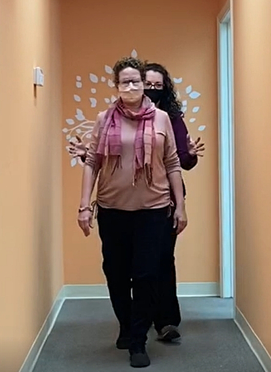 Walking with training prisms Two women walking in a hallway as part of a training exercise with prism glasses, with one person guiding the other from behind.